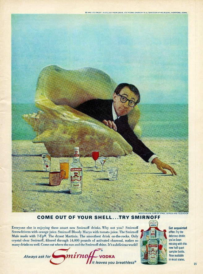 By the beach young Woody Allen, looking slightly apprehensive, holding a Smirnoff Vodka bottle with the text "Come out of your shell, try Smirnoff" nearby.